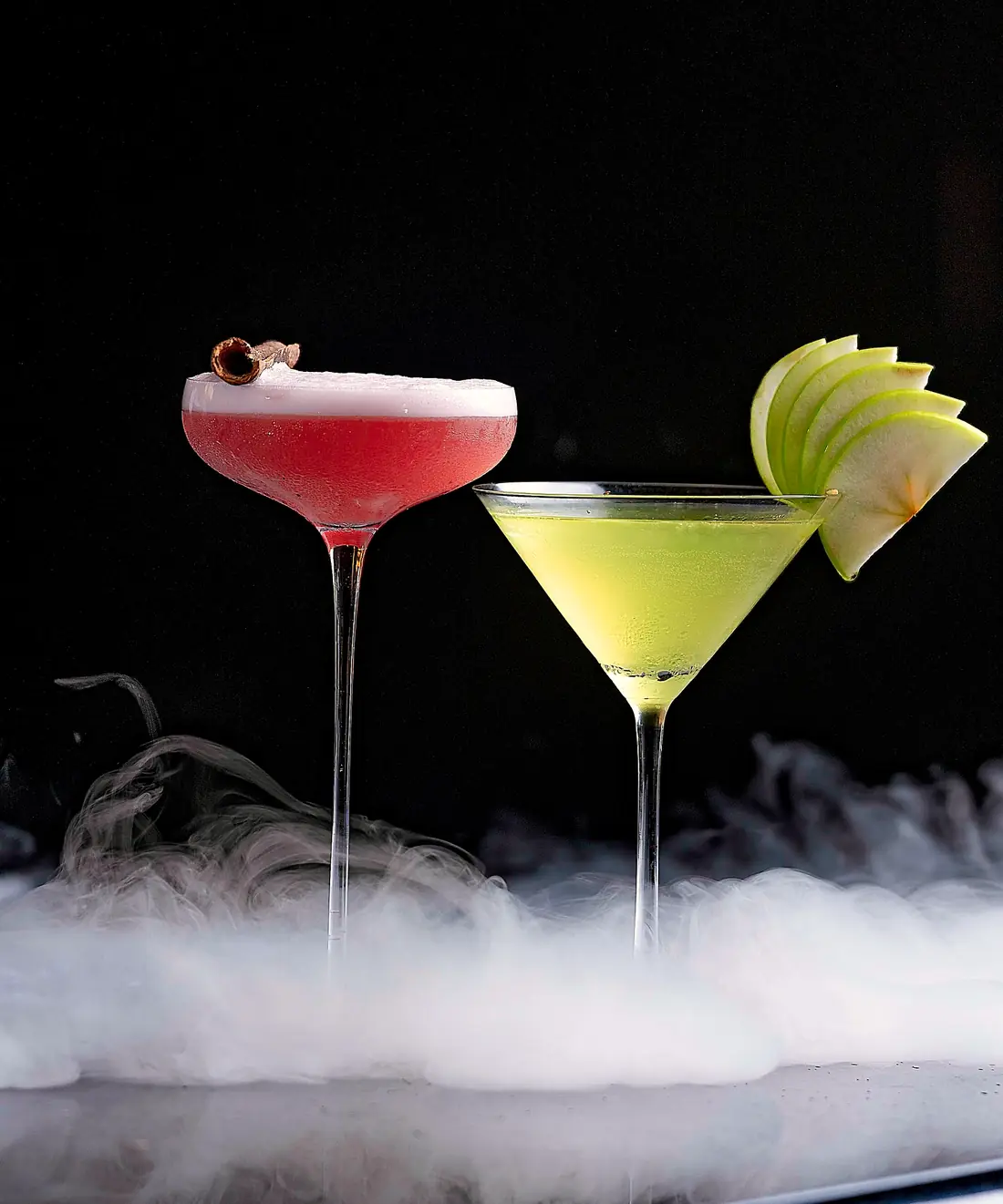Two cocktails over a low fog on the bar