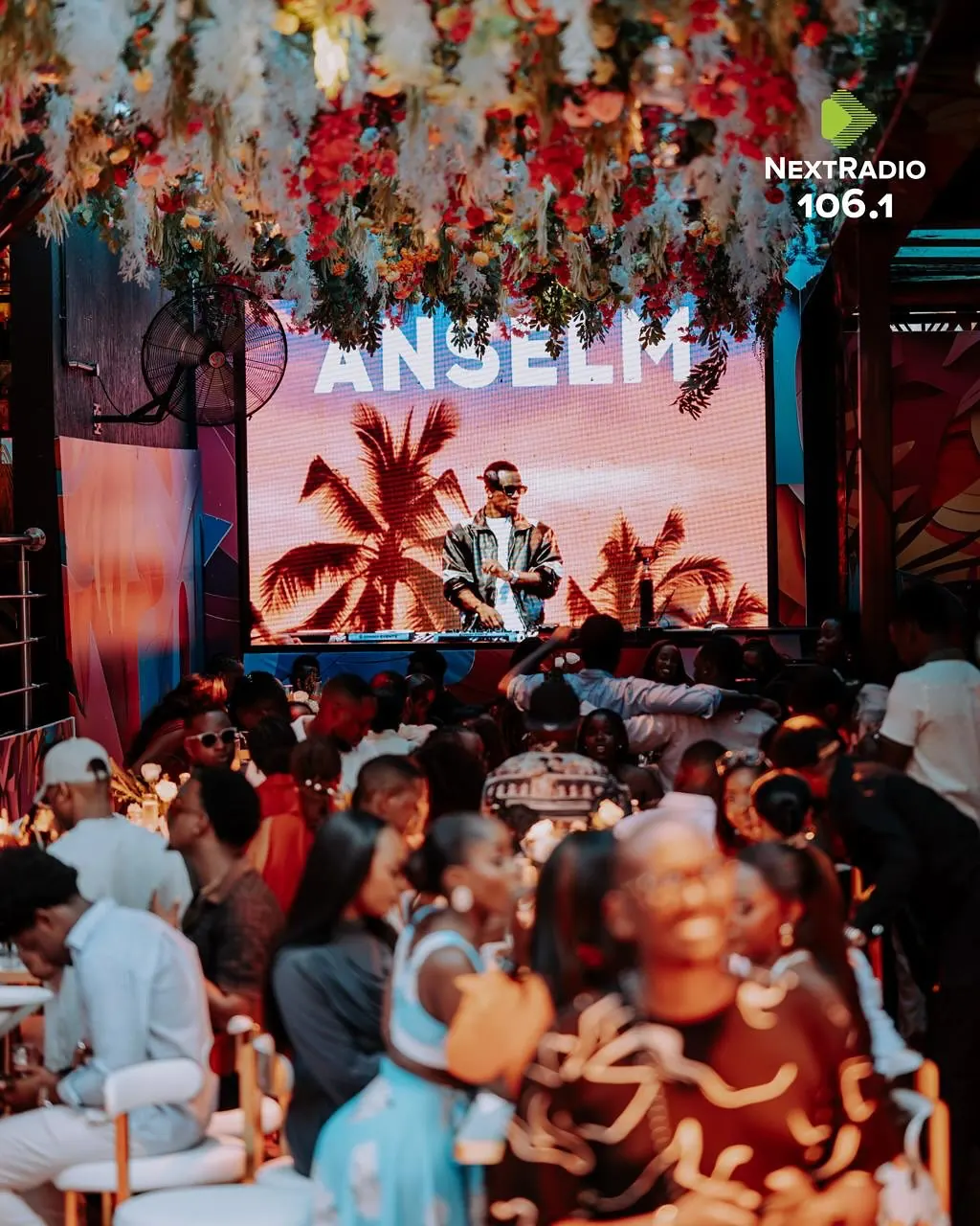 A DJ set under a ceiling of flowers, guests at long tables